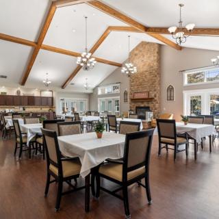 A spacious dining area with elegant chandeliers, wooden beams, and a stone fireplace.