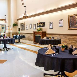 A neatly arranged dining area with round tables, each set with napkins and glassware, surrounded by artwork on the walls.