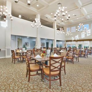 A spacious and elegantly designed dining room with several tables and chairs, featuring modern lighting fixtures and a patterned carpet.