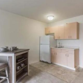 A minimalist apartment kitchen with basic amenities including a refrigerator, cabinets, and a small table.