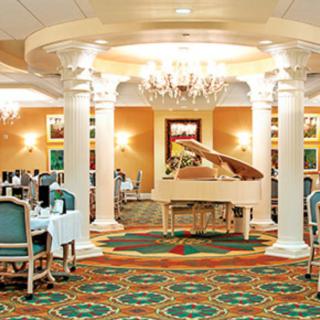 An elegant dining area with a grand piano, decorative chandeliers, and classic columns.