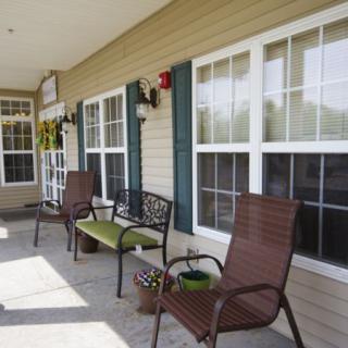 A cozy porch with chairs and a bench, adorned with plants next to large windows.