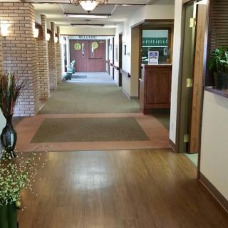 A well-lit hallway in a building with wood flooring and carpet, leading to a reception area.