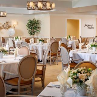 An elegantly set dining room with round tables, chairs, and floral centerpieces.