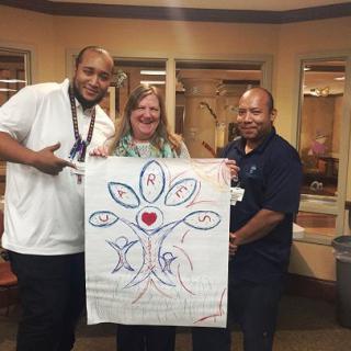 Three people holding a large drawing with a heart and colorful designs.