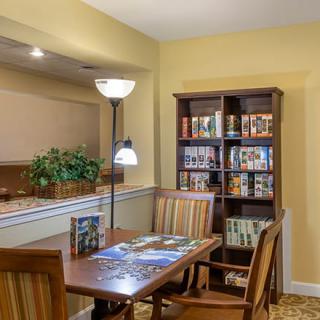 A cozy dining area with a wooden table, chairs, bookshelf, and floor lamp.
