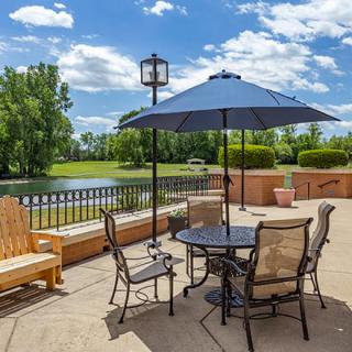 A scenic outdoor patio with a table, chairs, and umbrella overlooking a lake and trees.