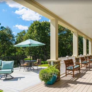 A sunny patio with outdoor seating and a large umbrella, surrounded by lush greenery.