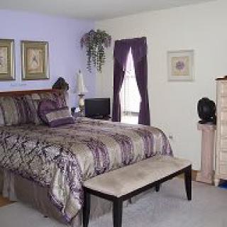 A cozy bedroom featuring a bed with purple accents, complemented by matching window curtains and decorative wall art.