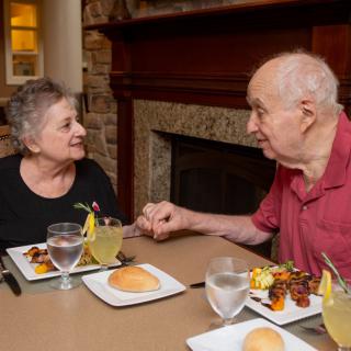 An elderly couple enjoying a meal together while holding hands at a restaurant.