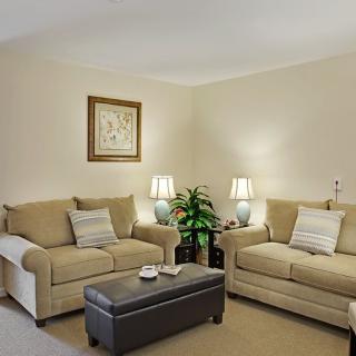 A cozy living room with beige sofas, a coffee table, and lamps providing soft lighting.