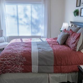 A neatly arranged bedroom with colorful bedding and ample natural light through the window.