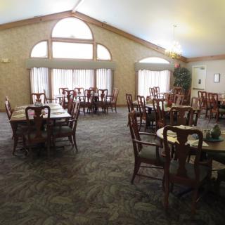 An empty dining room with multiple tables and chairs, featuring large windows and a carpeted floor.