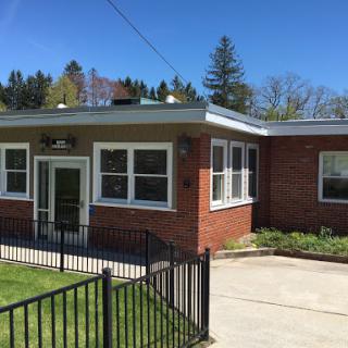 A well-maintained brick building with large windows and a fenced entry, surrounded by greenery on a sunny day.