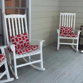 A cozy porch featuring white rocking chairs adorned with red patterned cushions, perfect for relaxation.