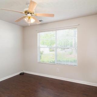 An empty room with wooden floors, a ceiling fan, and a window with blinds.