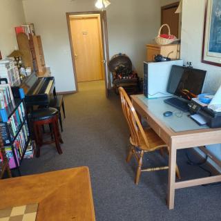 A cozy living room setup featuring a piano, computer desk, and bookshelf.