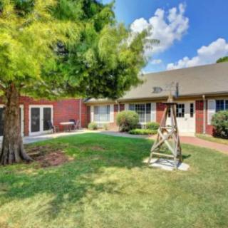 A picturesque backyard with a green lawn, a swing, and a brick house under a blue sky with clouds.
