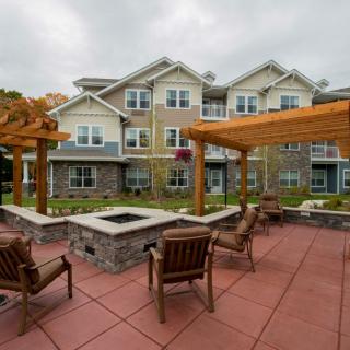 An inviting patio area with a fire pit and pergolas in front of a modern apartment building.