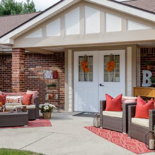 A cozy front porch with wicker furniture and red accents, perfect for relaxing outdoors.