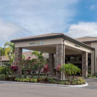 A modern building entrance surrounded by tropical landscaping and palm trees under a partly cloudy sky.
