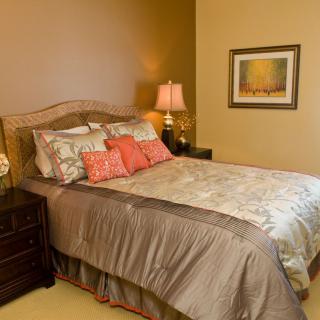A cozy bedroom with a neatly made bed, decorative pillows, and a warm lamp on the nightstand.
