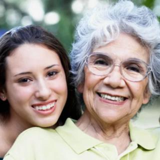 A grandmother and granddaughter smiling together outdoors.