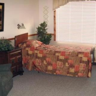A cozy bedroom with a bed covered in a patterned quilt, adjacent to a window with blinds and drapes.