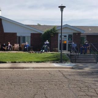 A group of people sitting outside a brick building on a sunny day.