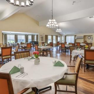 A spacious and elegantly furnished dining room with neatly arranged tables and chairs, featuring chandeliers.