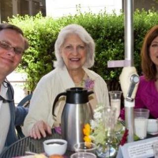 A group of three people smiling during an outdoor brunch.
