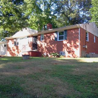 A suburban brick house with a spacious yard and surrounding trees.
