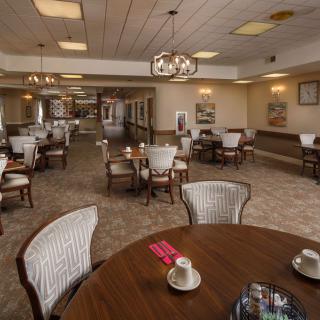 An elegantly decorated dining area with multiple tables and chairs, featuring chandeliers and carpeted floors.