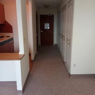 A view of a hallway in an apartment with a kitchen area visible on the left.