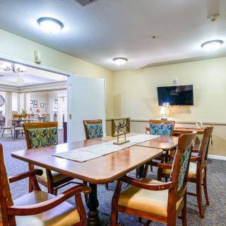 A well-lit dining room with a large table, chairs, and a wall-mounted television.
