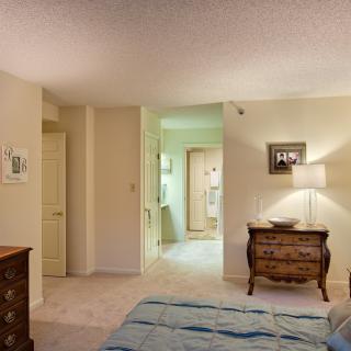 A cozy bedroom with a lamp and dresser, leading into an adjoining room.