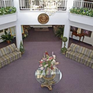 A spacious lobby featuring elegant furniture, a central floral arrangement, and a chandelier hanging from above.
