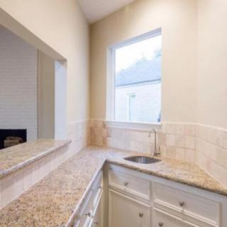 A bright kitchen area featuring a countertop with a sink, white cabinets, and a large window.