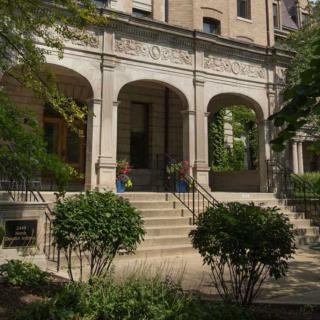 A historic building entrance with arched windows and lush greenery.