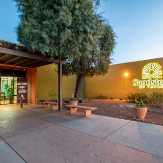 Entrance to a building illuminated in the evening, surrounded by landscaping.