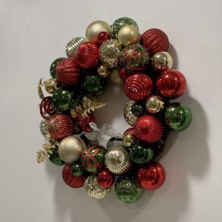 A festive Christmas wreath made of colorful ornaments in red, green, and gold.