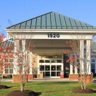 A symmetrical building entrance with a peaked roof and columns, surrounded by young trees.