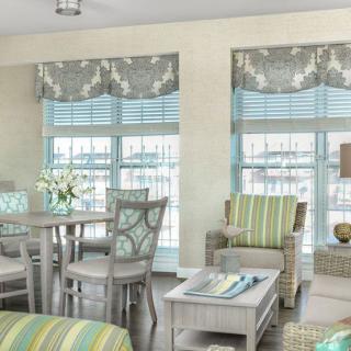 A bright and airy living room featuring pastel-colored furniture and large windows with patterned curtains.