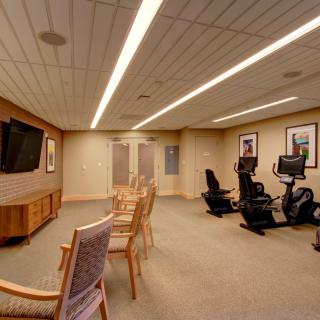 A cozy indoor fitness room with exercise equipment and chairs facing a television.