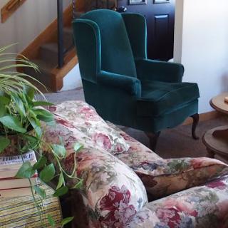 A cozy living room setup featuring a green armchair and a floral patterned sofa.