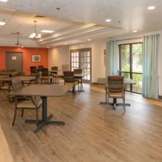 A spacious dining room with wooden tables and chairs, featuring large windows allowing natural light to fill the space.