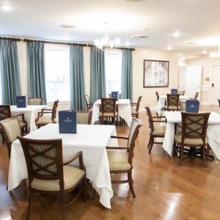 A neatly arranged dining room with tables set for guests, featuring elegant decor and large windows with blue curtains.