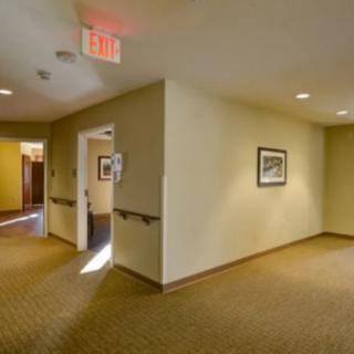 A well-lit hallway with cream-colored walls, featuring a doorway and an exit sign above it.