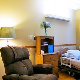 A cozy hospital room with a bed and recliner, featuring a lamp and a small shelf.