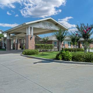 A beautifully landscaped building entrance with a covered driveway under a blue sky.